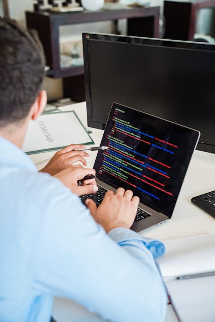 A close-up photograph of a computer screen displaying a code editor filled with multicoloured programming language syntax, including keywords, variables, functions, and symbols in shades of red, blue,